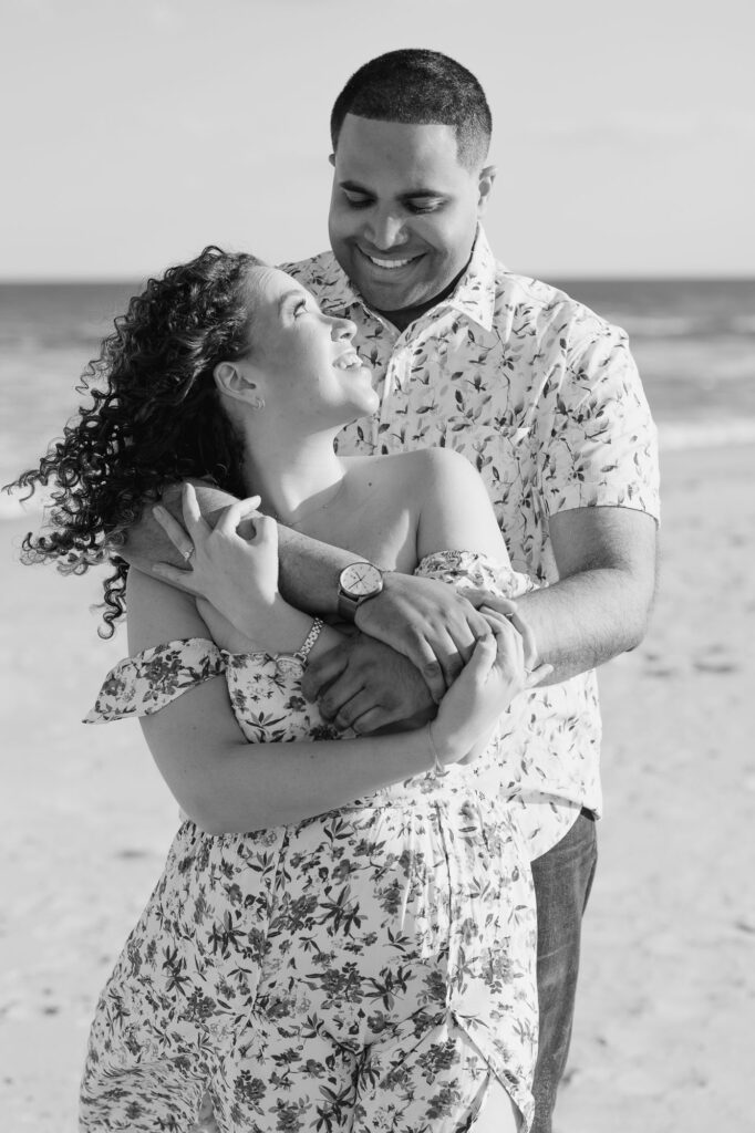 Black and white image of man and women posing  on beach and holding one another.  Photos taken by Simone Jaramillo Photography