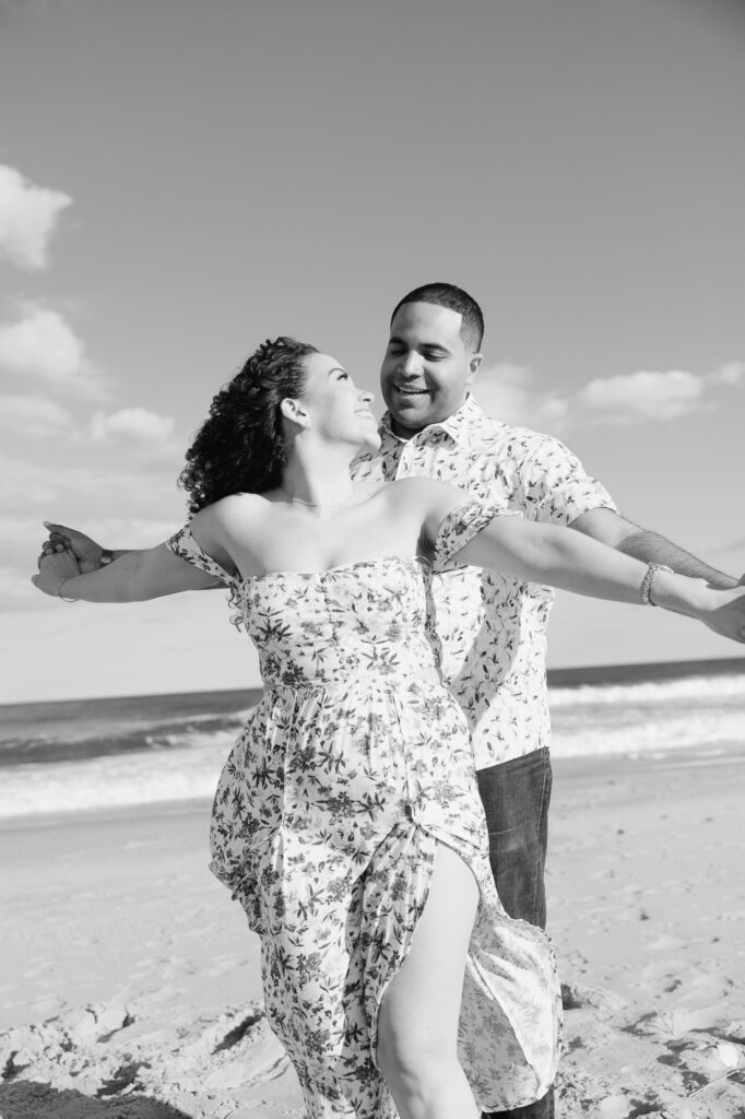 Black and white image of man and women share embrace on a beach in Spring Lake Beach, New Jersey.  Photo taken by Simone Jaramillo Photography