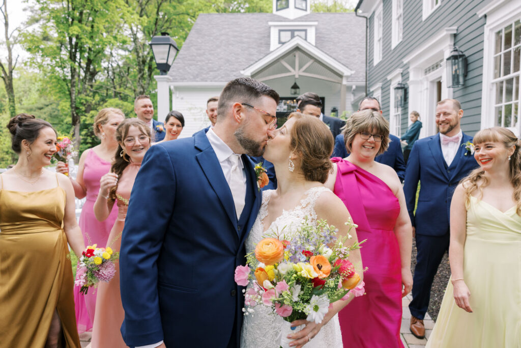 Couple kissing with bridal party behind them, Spring colored dress and florals