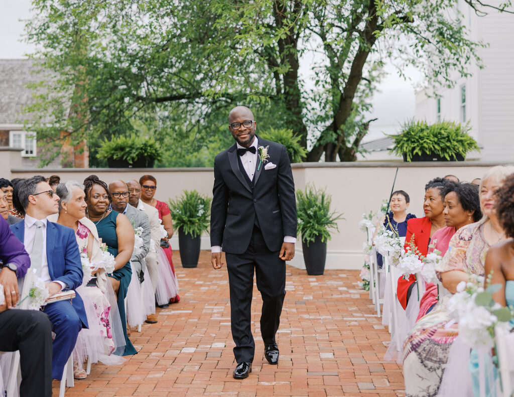 Groom in suit with bow tie walking down the aisle.  